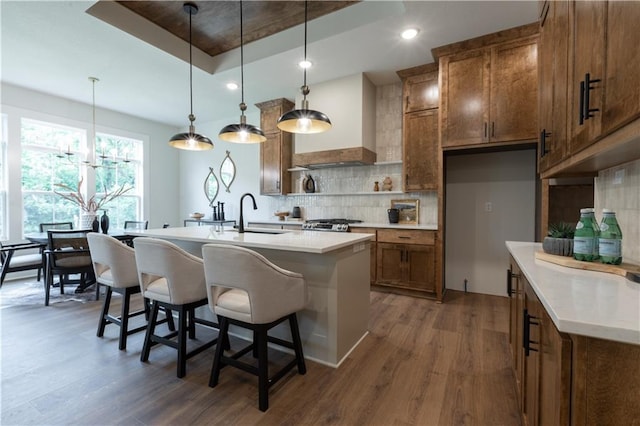 kitchen featuring sink, decorative light fixtures, a raised ceiling, custom range hood, and dark hardwood / wood-style floors