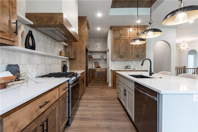 kitchen with stainless steel appliances, sink, light hardwood / wood-style flooring, hanging light fixtures, and a center island with sink