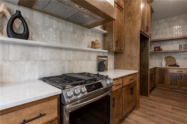 kitchen with gas range, light wood-type flooring, wall chimney range hood, and decorative backsplash