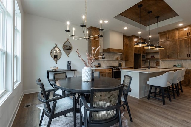 dining space featuring a raised ceiling, hardwood / wood-style flooring, a wealth of natural light, and a notable chandelier