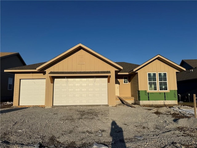 view of front of property featuring a garage, roof with shingles, board and batten siding, and gravel driveway