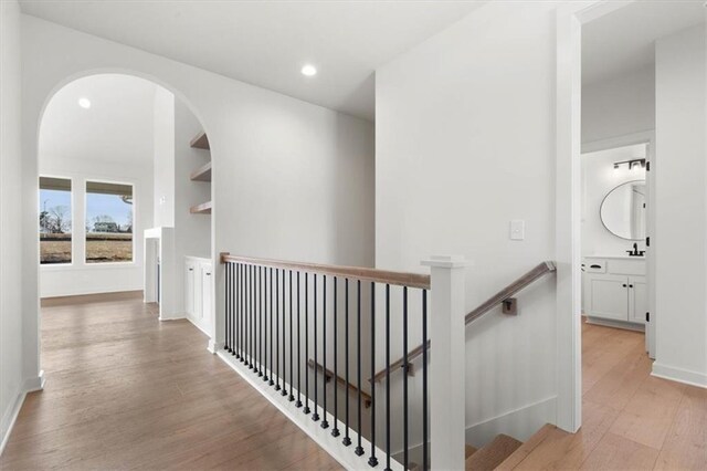 hallway with light wood finished floors, baseboards, an upstairs landing, and recessed lighting