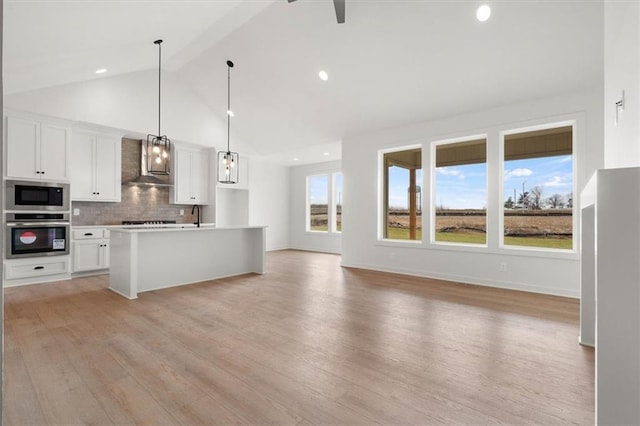 kitchen featuring light wood finished floors, stainless steel appliances, decorative backsplash, white cabinets, and wall chimney range hood