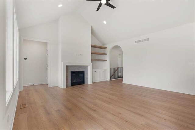 unfurnished living room with ceiling fan, high vaulted ceiling, a tile fireplace, light wood-style flooring, and visible vents