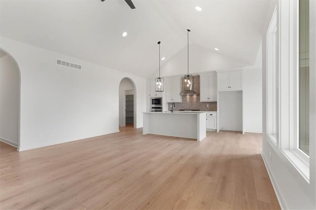 unfurnished living room with light wood finished floors, visible vents, arched walkways, a ceiling fan, and a sink