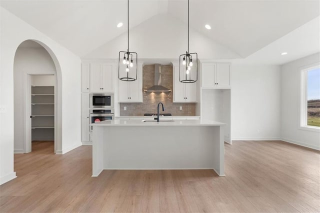 kitchen featuring wall chimney range hood, built in microwave, light countertops, and arched walkways