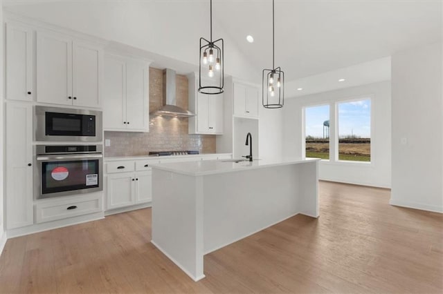 kitchen featuring oven, a sink, light countertops, built in microwave, and wall chimney exhaust hood