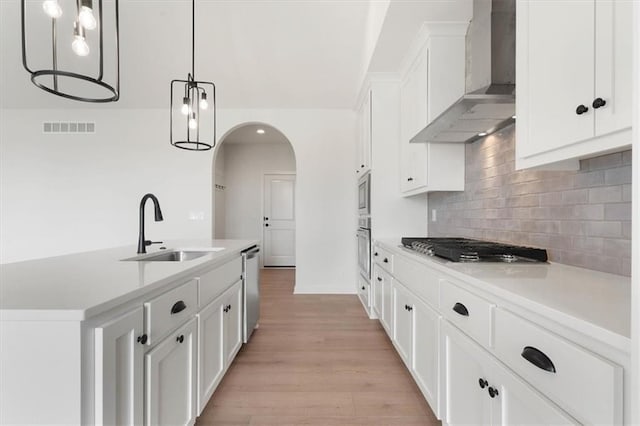 kitchen featuring visible vents, wall chimney exhaust hood, appliances with stainless steel finishes, light countertops, and a sink