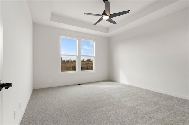 unfurnished room with carpet floors, baseboards, a tray ceiling, and a ceiling fan