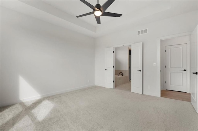 unfurnished bedroom featuring light carpet, baseboards, visible vents, a raised ceiling, and a ceiling fan