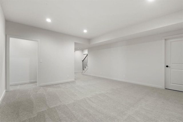 empty room featuring recessed lighting, light colored carpet, baseboards, and stairs