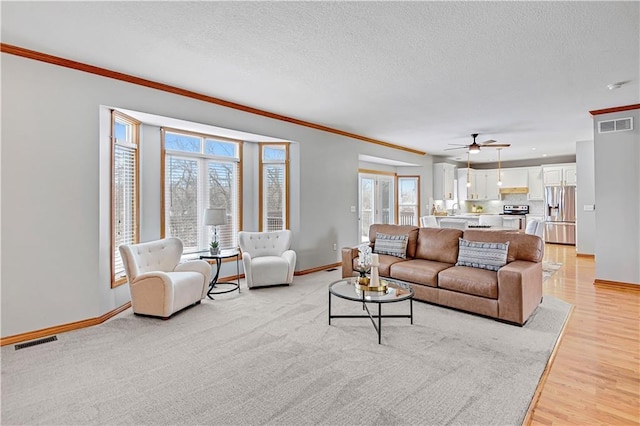 living room featuring a wealth of natural light, light hardwood / wood-style flooring, ornamental molding, and a textured ceiling