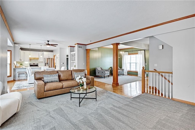 living room with decorative columns, light colored carpet, ornamental molding, and ceiling fan