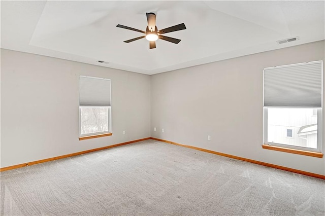 empty room with ceiling fan, carpet floors, and a tray ceiling