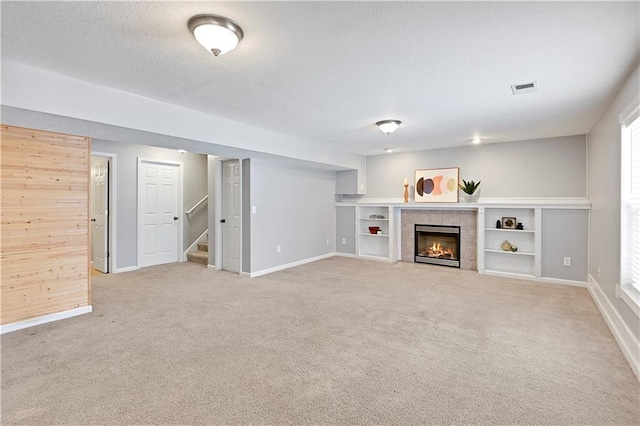 unfurnished living room with light colored carpet, a tile fireplace, and wooden walls