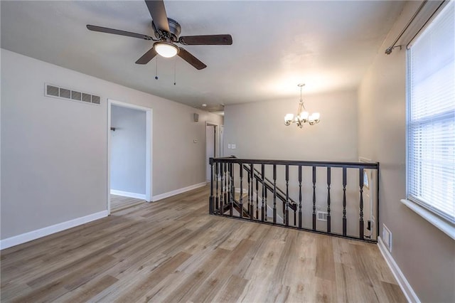 spare room featuring ceiling fan with notable chandelier and light hardwood / wood-style floors