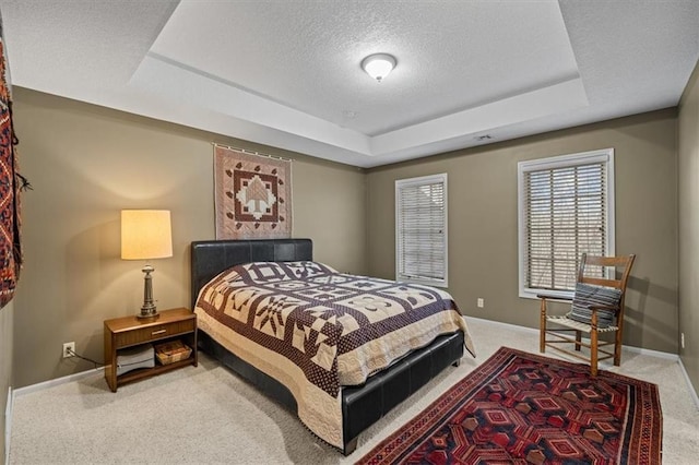 bedroom with carpet flooring, a textured ceiling, and a tray ceiling