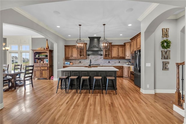 kitchen featuring a kitchen breakfast bar, backsplash, a kitchen island with sink, and custom exhaust hood