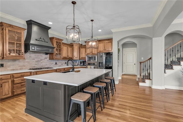 kitchen with a kitchen bar, appliances with stainless steel finishes, premium range hood, tasteful backsplash, and a kitchen island with sink