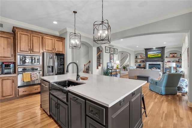 kitchen with appliances with stainless steel finishes, ornamental molding, sink, a center island with sink, and an inviting chandelier