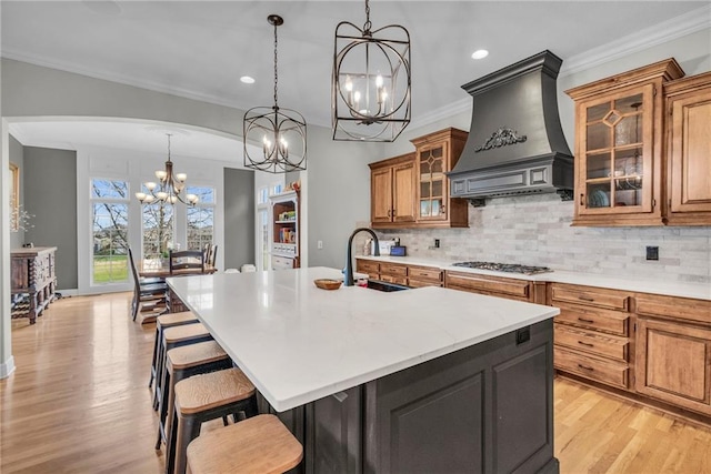 kitchen with sink, backsplash, a large island with sink, stainless steel gas stovetop, and custom range hood