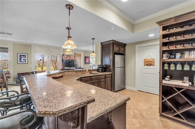 kitchen with decorative light fixtures, stainless steel fridge, dark brown cabinets, and a breakfast bar