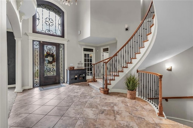 tiled entryway featuring a towering ceiling, decorative columns, an inviting chandelier, and ornamental molding