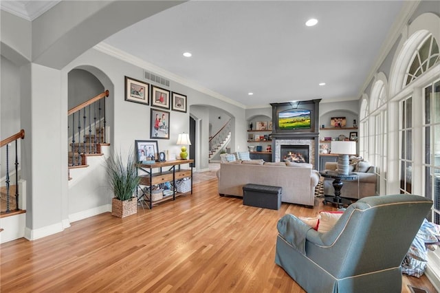 living room featuring a fireplace, light hardwood / wood-style flooring, built in features, and ornamental molding