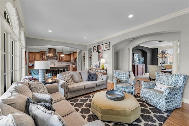 living room featuring decorative columns, crown molding, wood-type flooring, and a notable chandelier