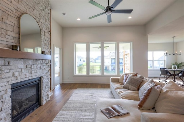 living room featuring a stone fireplace, ceiling fan with notable chandelier, and hardwood / wood-style flooring