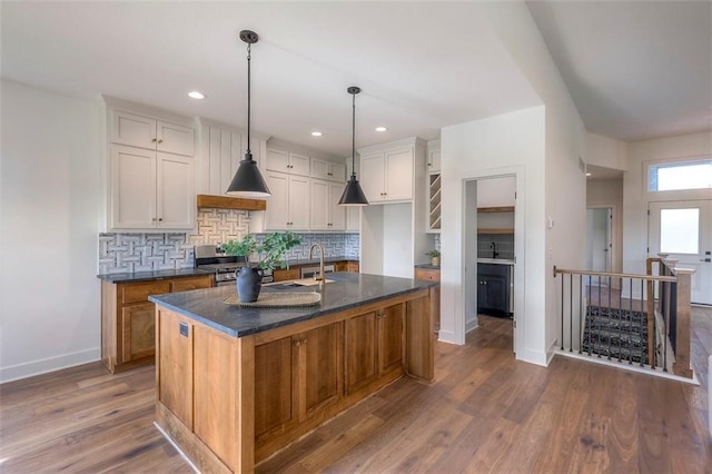 kitchen featuring a center island with sink, decorative backsplash, decorative light fixtures, white cabinetry, and wood-type flooring