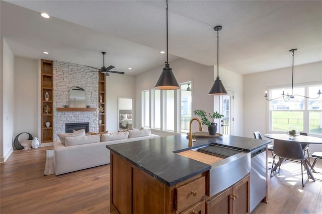 kitchen featuring a center island with sink, hanging light fixtures, hardwood / wood-style flooring, built in features, and a fireplace