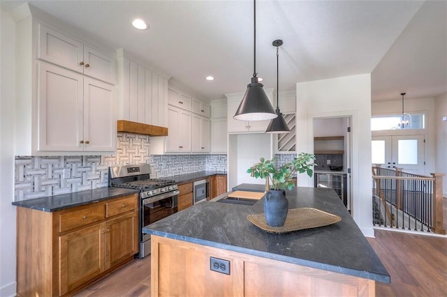 kitchen with decorative light fixtures, white cabinetry, stainless steel gas range oven, and a kitchen island with sink