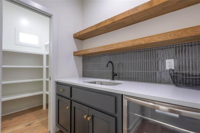 bar with decorative backsplash, light wood-type flooring, beverage cooler, and sink