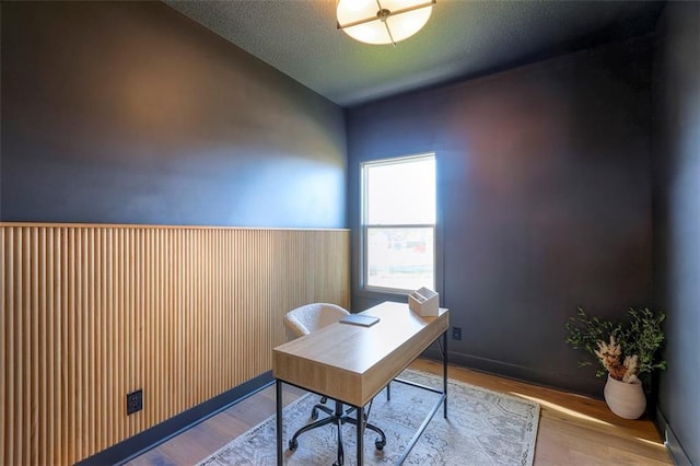 home office featuring vaulted ceiling, a textured ceiling, wooden walls, and light hardwood / wood-style flooring