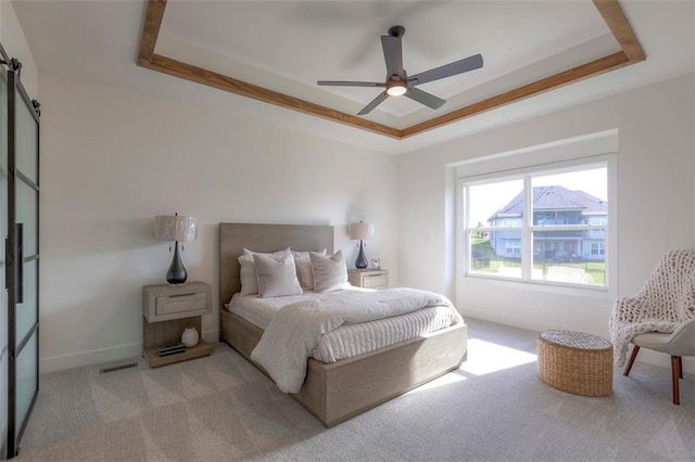 bedroom with a tray ceiling, a barn door, ceiling fan, and light colored carpet