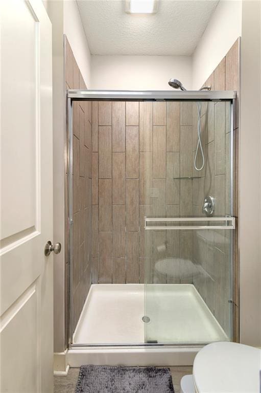 bathroom with toilet, a shower with door, and a textured ceiling