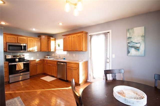 kitchen featuring light wood-type flooring, stainless steel appliances, backsplash, and sink