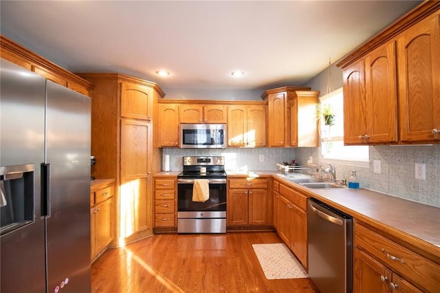 kitchen featuring light wood-type flooring, appliances with stainless steel finishes, decorative backsplash, and sink