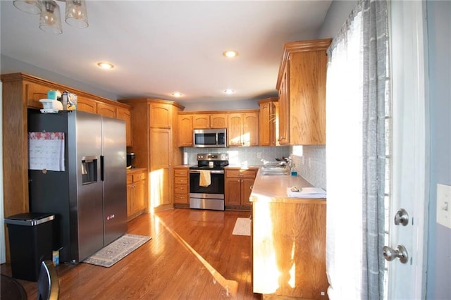 kitchen featuring appliances with stainless steel finishes, light hardwood / wood-style flooring, tasteful backsplash, and sink