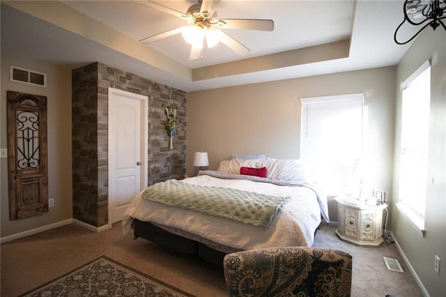 carpeted bedroom featuring ceiling fan, a tray ceiling, and multiple windows