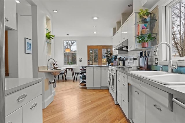 kitchen with light wood-type flooring, sink, white cabinets, stainless steel stove, and hanging light fixtures