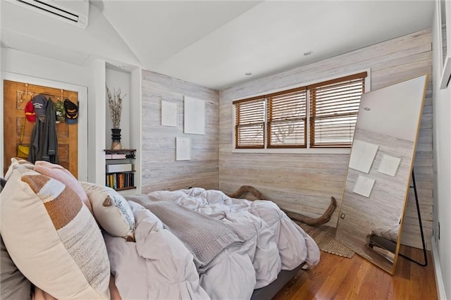 bedroom featuring hardwood / wood-style flooring, a wall mounted air conditioner, wooden walls, and vaulted ceiling