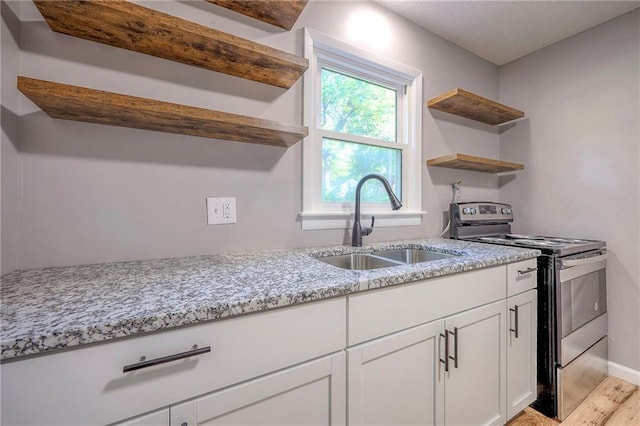 kitchen featuring light stone counters, sink, light hardwood / wood-style flooring, white cabinetry, and stainless steel electric range