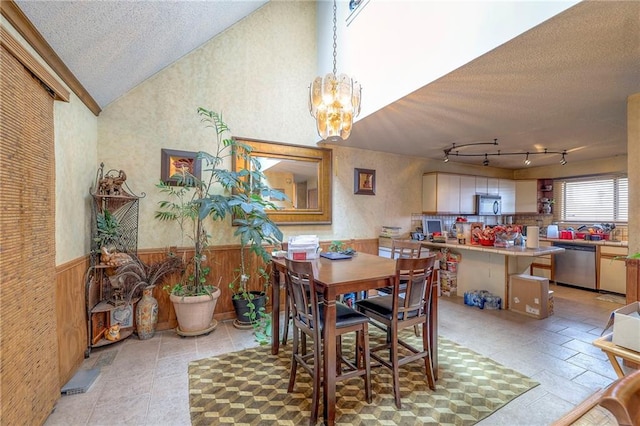 dining area with a notable chandelier, wood walls, vaulted ceiling, track lighting, and a textured ceiling