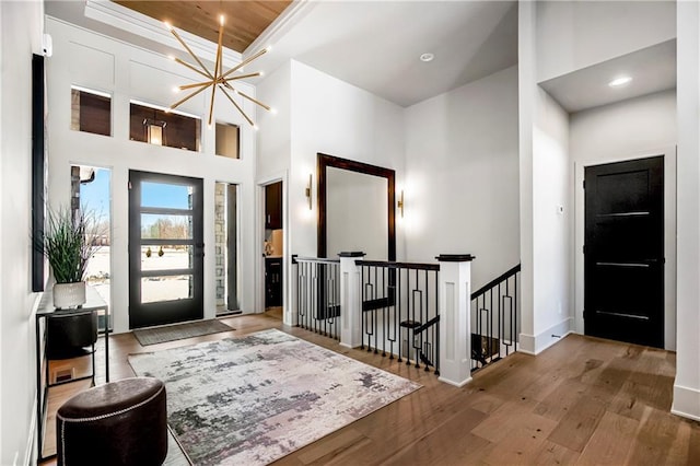 entrance foyer with a notable chandelier, recessed lighting, a towering ceiling, wood finished floors, and baseboards