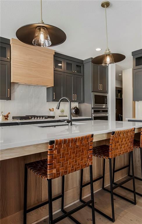 16781 S Fellows St, Olathe, KS 66062 - kitchen with stainless steel appliances, light countertops, pendant lighting, light wood-style flooring, and glass insert cabinets