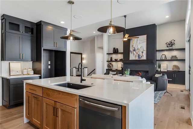 16781 S Fellows St, Olathe, KS 66062 - kitchen featuring stainless steel dishwasher, light wood-style flooring, a glass covered fireplace, open floor plan, and an island with sink