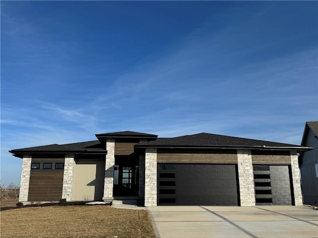 prairie-style home with an attached garage, stone siding, driveway, and roof with shingles