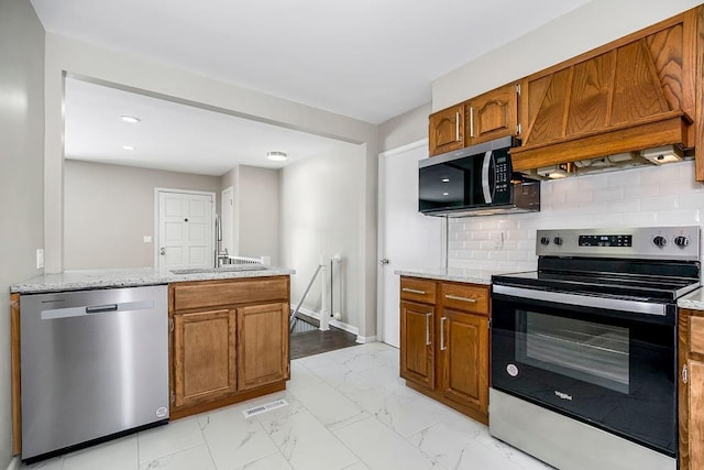 kitchen with stainless steel appliances, sink, light stone counters, and decorative backsplash